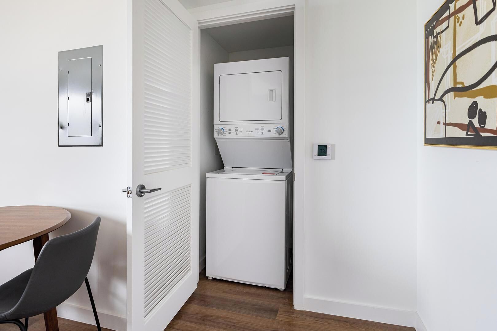Une petite buanderie comprenant un lave-linge et un sèche-linge, une porte avec une poignée et une petite table avec une chaise.