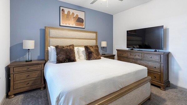 A neatly arranged bedroom with a large bed, a television, and a dresser.