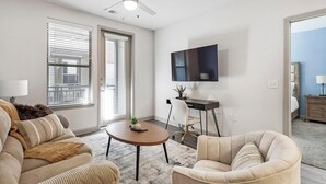 Een moderne woonkamer met een bank, fauteuil, salontafel en een aan de muur bevestigde televisie.