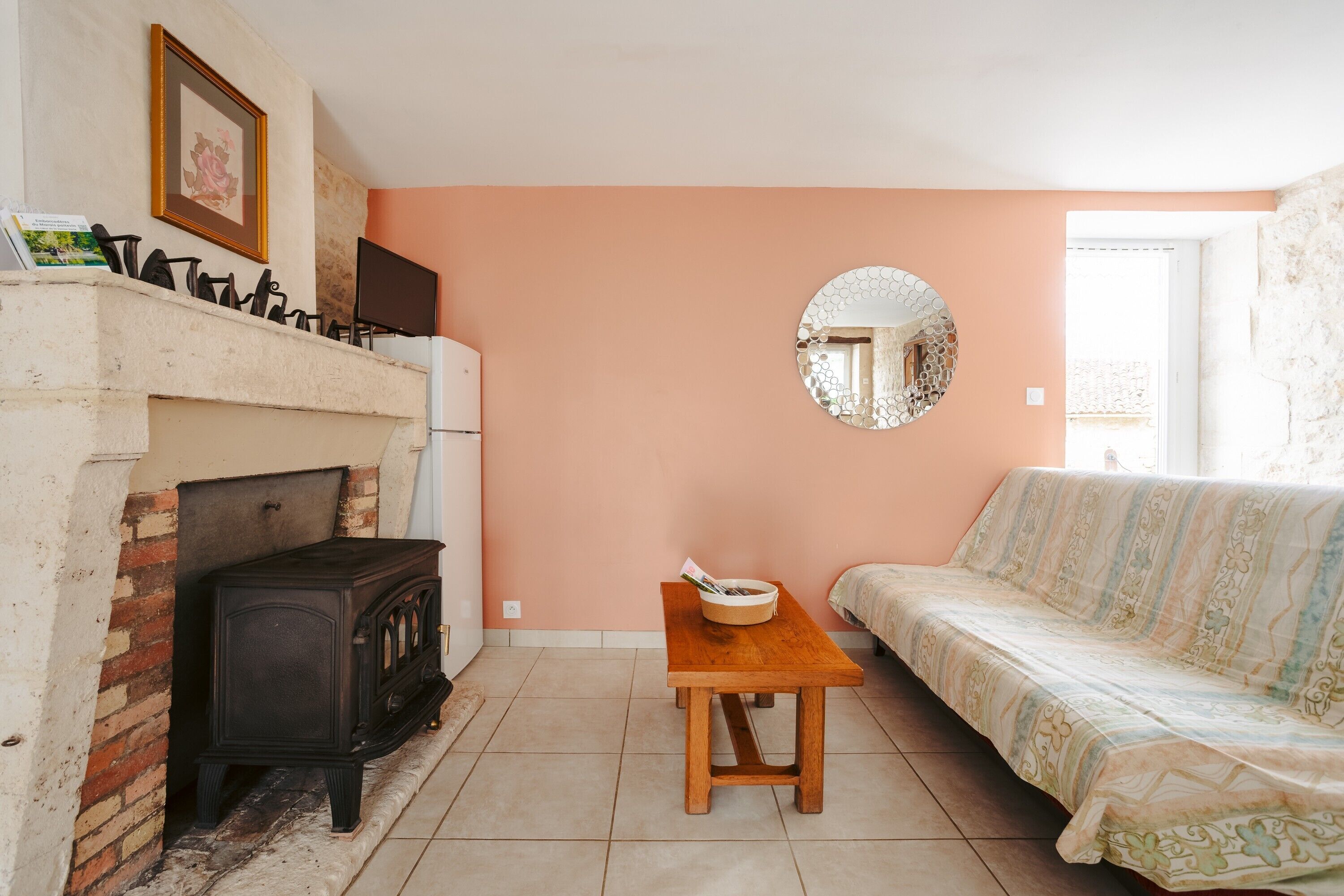 Een woonkamer met een open haard, een bank, een houten tafel en een ronde spiegel aan de muur.