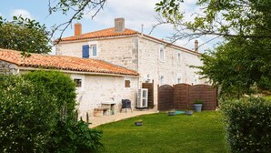 Una casa de piedra con techo de tejas, patio cercado y un pequeño jardín.