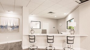 A modern kitchen with a white countertop, three bar stools, a clock, and a window with a view. - Landing | Stylish Studio, Courtyard, Gym (Port Charlotte)