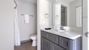 A modern bathroom with a white toilet, a shower with a curtain, a large mirror, and a vanity with a sink and cabinet. - Landing | Beautiful Studio, Gym, Courtyard (Port Charlotte)