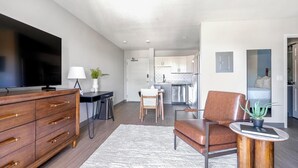 A modern living room with a TV, wooden dresser, and a dining area with a table and chairs. - Landing | Stylish Studio, Courtyard, Gym (Port Charlotte)