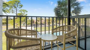 A balcony with wicker chairs and a small table, overlooking a parking area and greenery. - Landing | Stylish Studio, Courtyard, Gym (Port Charlotte)