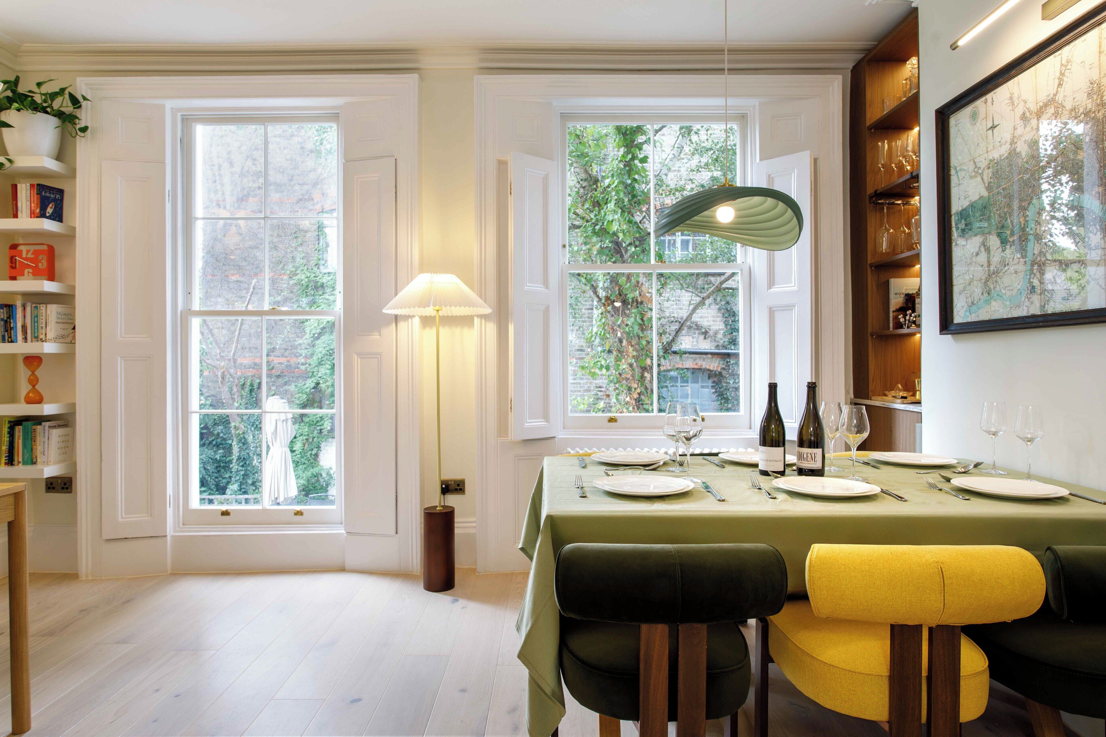 A dining area with a table set for four, a lamp, and a view of greenery outside.