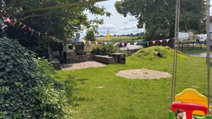 A grassy outdoor area with a swing set, a barbecue grill, and a play structure.