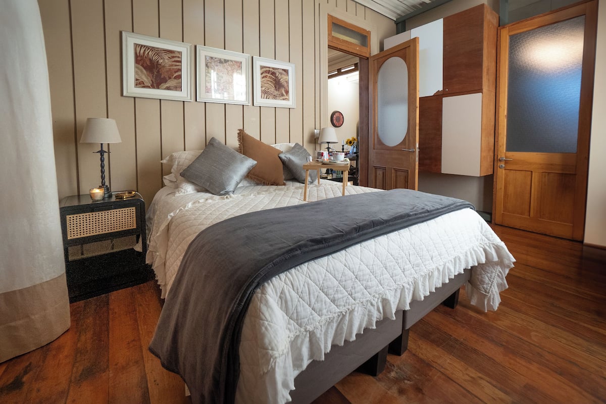 Une chambre à coucher avec un lit, une table de chevet, une lampe et une œuvre d’art encadrée accrochée au mur.