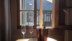 A table with two empty wine glasses and a copper champagne bucket with a bottle inside, positioned by a window with a view of buildings. - Departamentos Puerto Claro (Valparaíso)