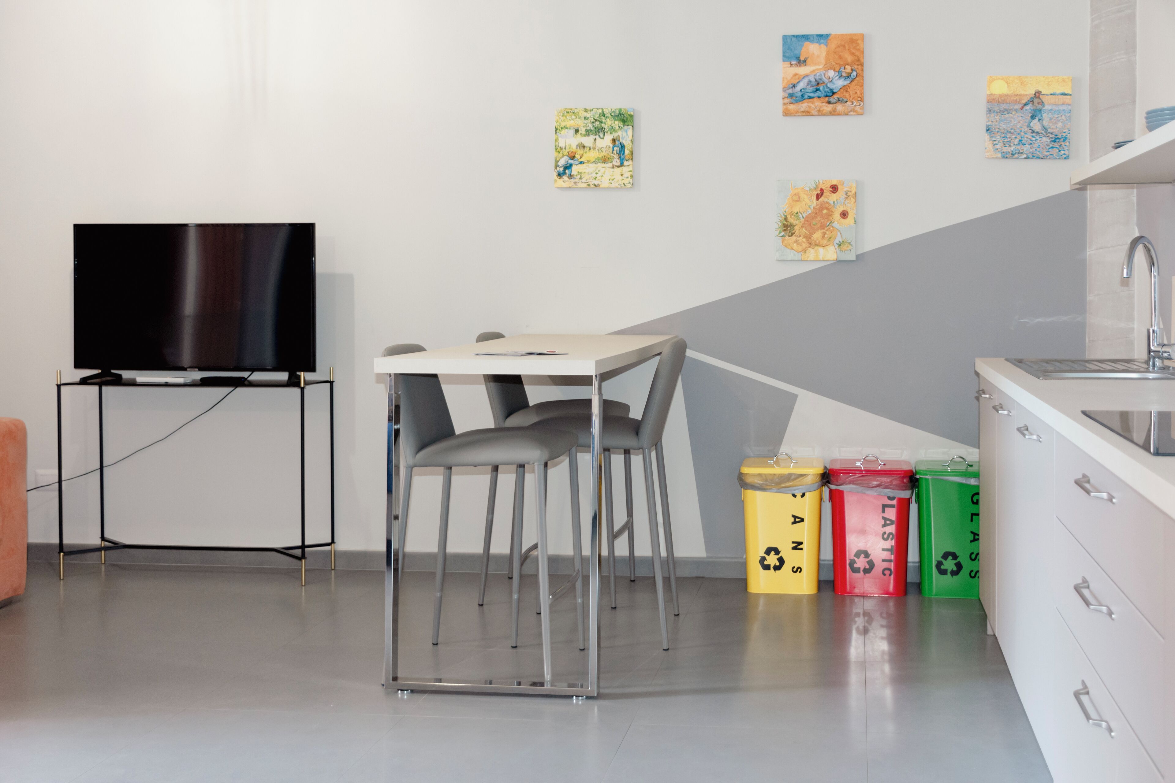A modern kitchen with a dining area, a flat-screen TV, and recycling bins.