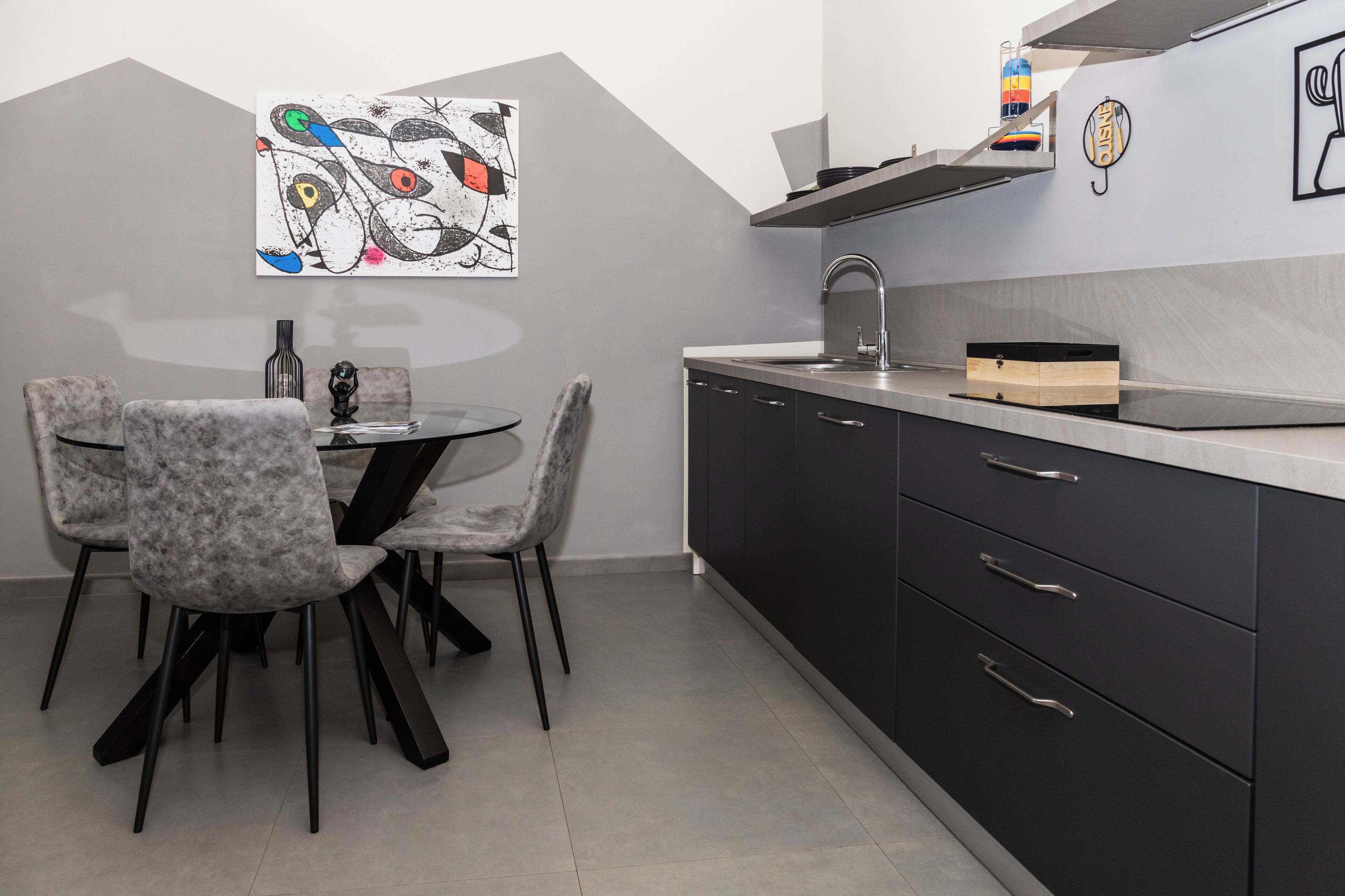 A modern kitchen with a dining area, featuring a marble countertop, black cabinets, and a unique abstract painting on the wall.
