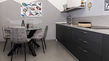 Una cocina moderna con comedor, que presenta una encimera de mármol, gabinetes negros y un cuadro abstracto único en la pared.