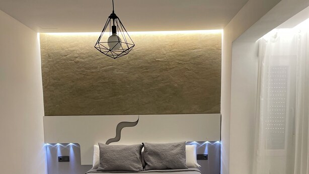 Une chambre à coucher moderne avec un grand lit, un luminaire aux formes géométriques et une petite table de chevet agrémentée d’une plante.