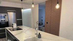 Une cuisine moderne dotée d’un plan de travail en marbre, d’appareils électroménagers en acier inoxydable et de luminaires suspendus.