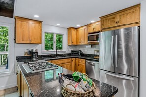 Une cuisine moderne avec des meubles en bois, des appareils en acier inoxydable, un plan de travail en granit et une vue sur l’extérieur.
