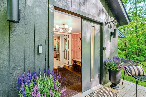 A wooden exterior with a door leading to an interior with a chandelier and a bench.