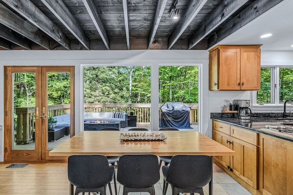 A modern kitchen with wooden cabinets, a dining area with a large table and chairs, and a view of a lush garden through large windows.