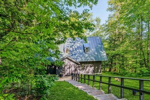 A rustic cabin with a wooden exterior, a metal roof, and a wooden staircase leading to the entrance.