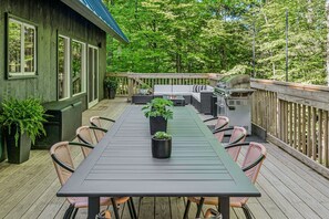 A wooden deck with a table and chairs, a grill, and potted plants.