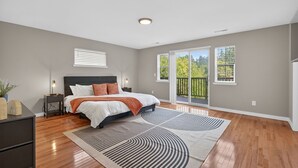 A bedroom with a bed, a nightstand, a dresser, a large window, and a balcony.