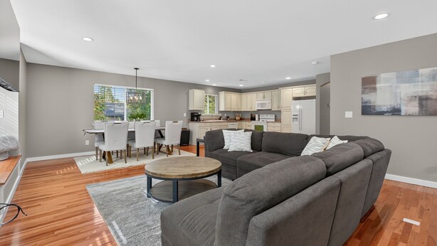 A modern living room with a gray sectional sofa, a round coffee table, and a dining area with a white table and chairs.