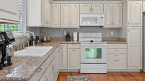 A kitchen with white cabinets, a granite countertop, a built-in microwave, and a stainless steel oven.