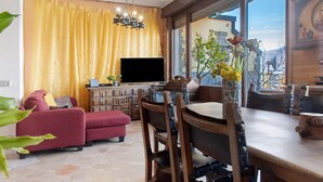 Ein Wohnzimmer mit einer Couch, einem Fernseher, einem Holzesstzimmer und Stühlen, sowie einem Fenster mit Blick.