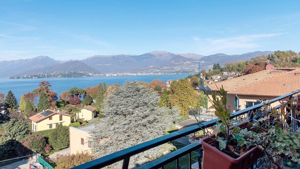 Ein Wohngebiet mit Häusern, einem Balkon mit Topfpflanzen und Blick auf einen See und Berge.