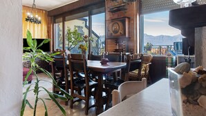 Ein Essbereich mit Holzmöbeln, einer Chandelüster und Blick auf Berge durch große Fenster.