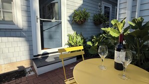 Um pátio com mesa e cadeiras amarelas, uma garrafa de vinho e plantas em vasos.