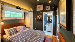Quarto com cama, janela, porta para o banheiro e parede com quadros.