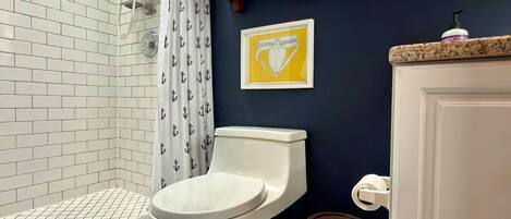 A bathroom with a white toilet, a shower with a white tiled wall, and a blue accent wall.