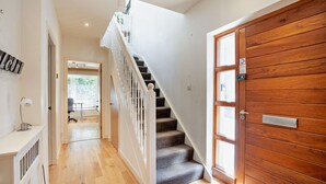 Un couloir avec une porte en bois, un escalier et un bureau avec une lampe.