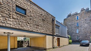 Un bâtiment en pierre avec une extension moderne, une voiture garée devant et une allée pavée.