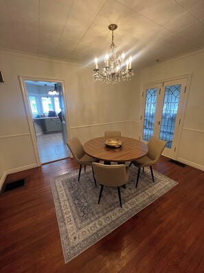 A dining area with a round table, four chairs, a chandelier, and a patterned rug.