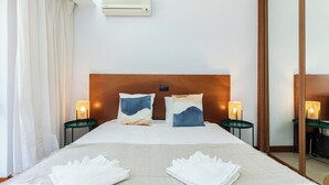 A hotel room with a large bed, two bedside tables, a headboard, an air conditioning unit, and a mirror. - Palm White Apartment, Vilamoura, Algarve (Quarteira)