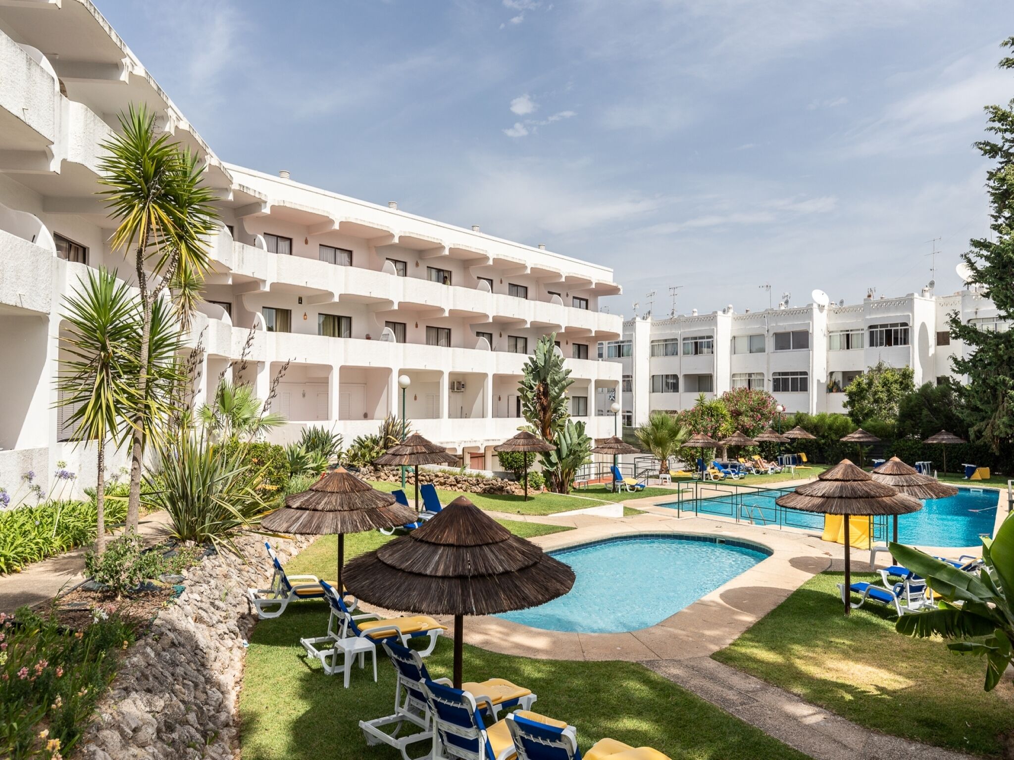A hotel with multiple balconies, a swimming pool, and sun loungers.