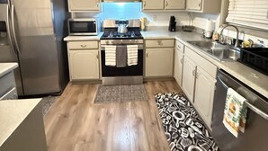 Une cuisine compacte avec un revêtement de sol en bois clair, un réfrigérateur en acier inoxydable, une cuisinière à gaz et des armoires blanches.
