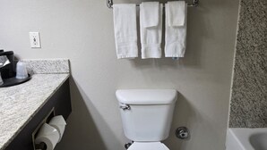 A bathroom with a toilet, a towel rack with towels, a toilet paper holder, and a sink with a countertop.