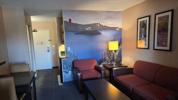 A hotel room with a sofa, armchair, and a small table. There is a painting of a landscape on the wall.