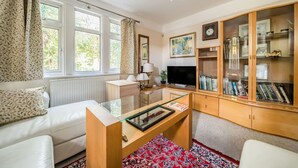A well-lit living room with a sofa, a glass coffee table, a television, and a bookcase filled with books and decorative items. - Spacious 4-bed, 4-bath home with garden and parking (Berkshire)