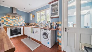A compact kitchen with a built-in oven, a washing machine, and a tiled backsplash. - Spacious 4-bed, 4-bath home with garden and parking (Berkshire)