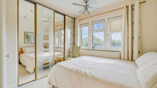 A bedroom with a large bed, a chair, a ceiling fan, and a sliding door leading to another room. - Spacious 4-bed, 4-bath home with garden and parking (Berkshire)