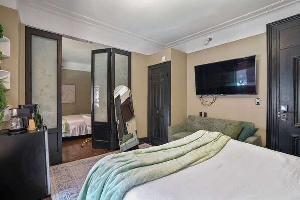 A bedroom with a bed, a television mounted on the wall, a desk with a lamp, and a mirror.