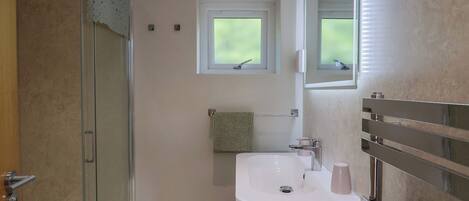 Un bagno con una cabina doccia in vetro, un lavabo con uno specchio sopra e una finestra sopra il lavabo.