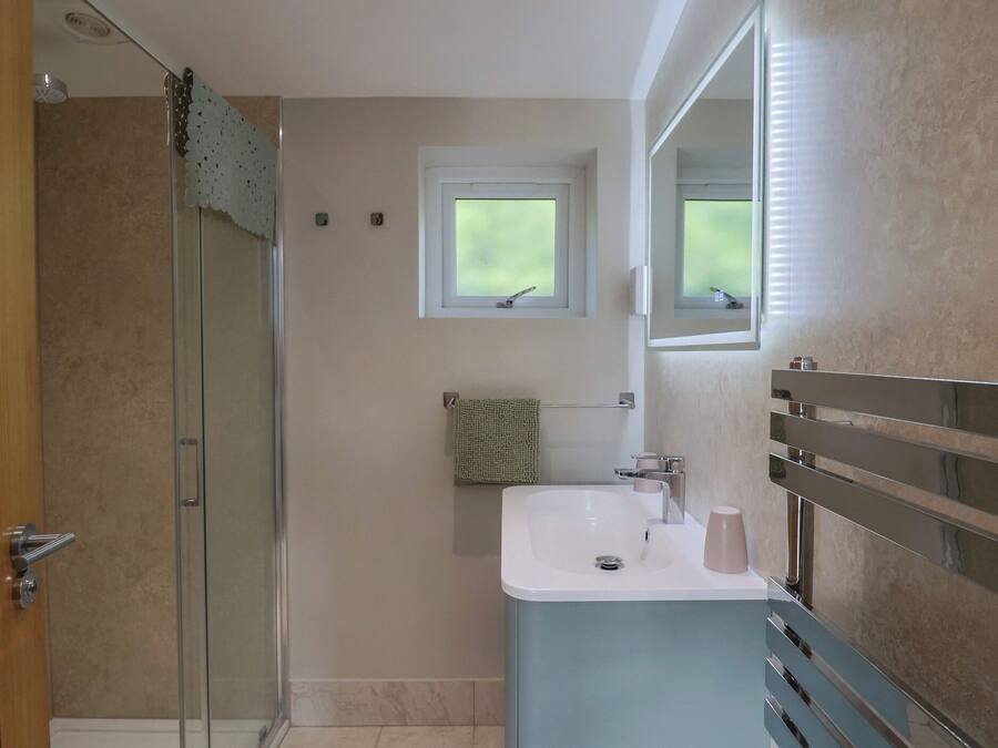 A bathroom with a glass shower door, a sink with a mirror above it, and a window above the sink.