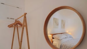 Ein Schlafzimmer mit einem Wäscheständer aus Holz, der weiße Handtücher trägt, einem runden Spiegel an der Wand und einem Bett mit weißer Bettwäsche.