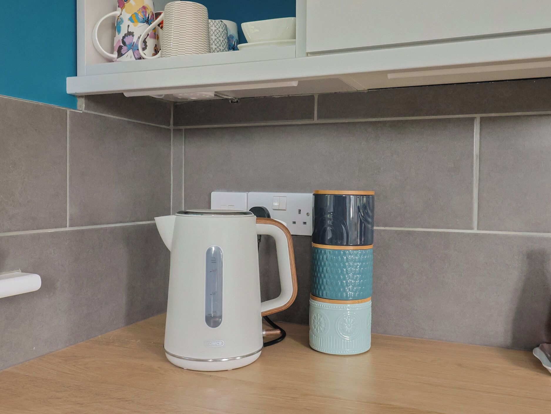Cozinha com chaleira, pilha de canecas e tomada.