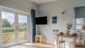 Ein Essbereich mit Holztisch und -stühlen, einem an der Wand befestigten Fernseher und Blick ins Freie durch eine Glastür.