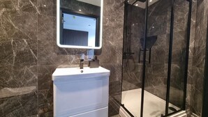 Ein modernes Badezimmer mit Marmorwand, einem weißen Waschbecken, einer Glasdusche und einem Spiegel mit integrierter Beleuchtung.